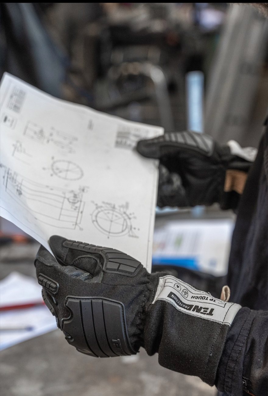 Gloved hands holding engineering drawings on the shop floor